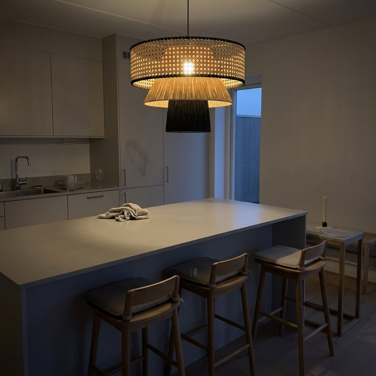 Rylie Rattan Black Pendant Light over kitchen island, smaller tiered drums in a row keeping sightlines open across the counter for prep work