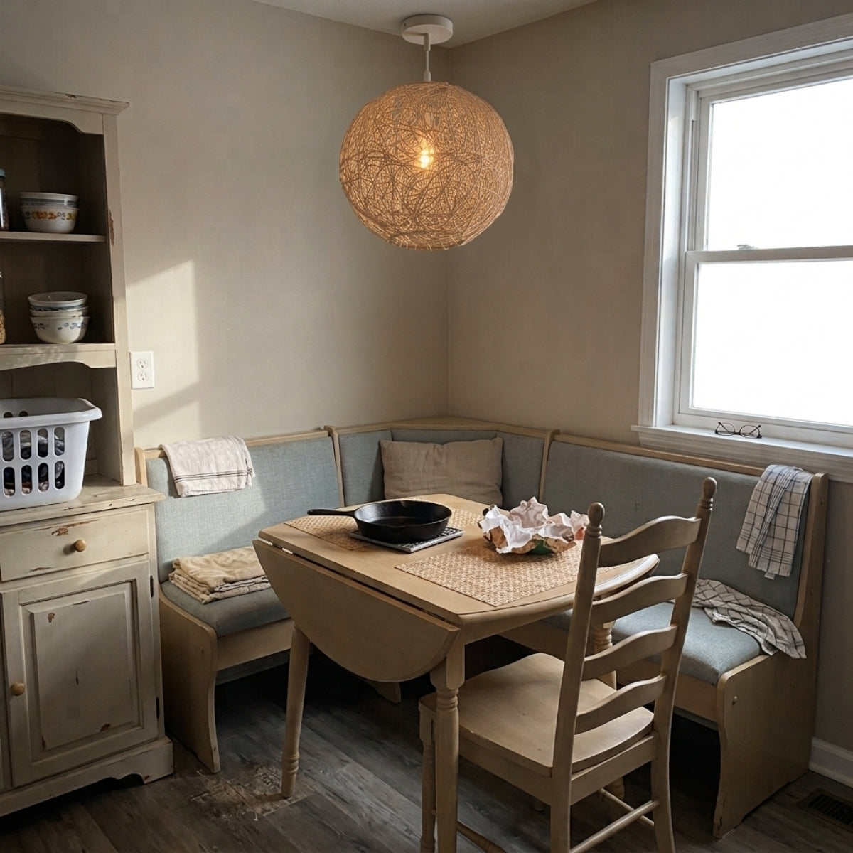 Sucada Round Rattan Ceiling Light Fixture above dining table, cocoon sphere scattering warm light across place settings through its open nest weave without glare