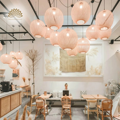 Many Lucy round woven bamboo pendant lights hang over small wooden tables in a modern, cozy cafe.
