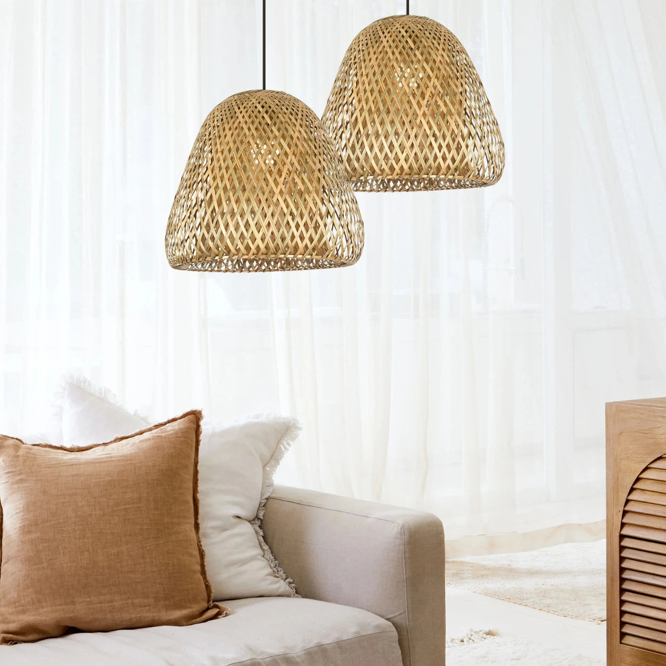 Two bell-shaped Beirut-woven pendant lights hang over a cozy beige sofa in a bright Boho room